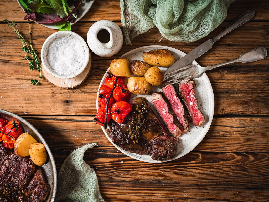 Steak z vysokého roštěnce s pečenými bramborami, rajčaty a pepřovou omáčkou